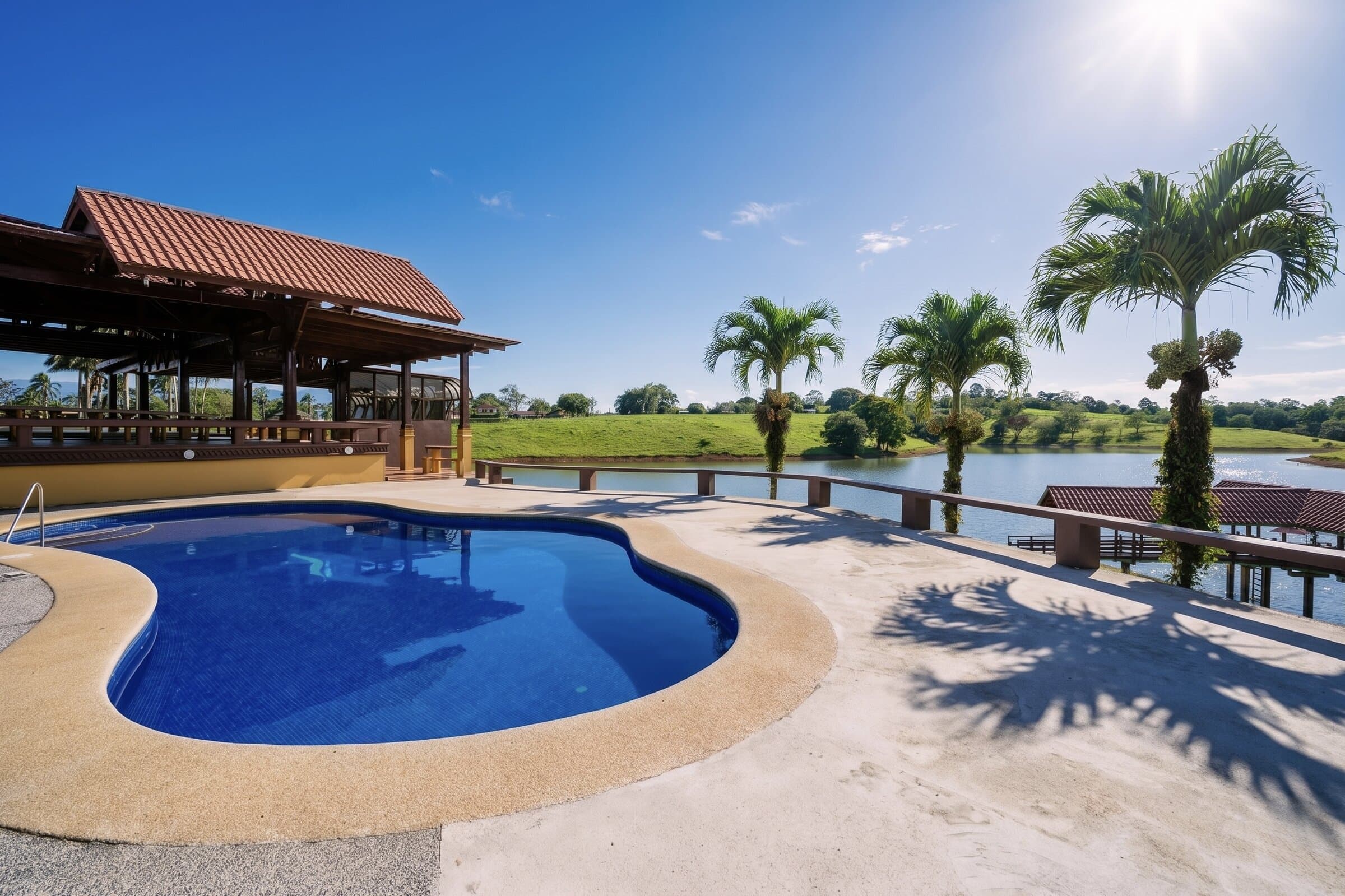 Piscina con vista al lago, palmeras y arena clara al borde